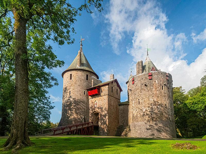 Castell Coch, framed against a bright blue sky with some clouds, with a tree in the foreground