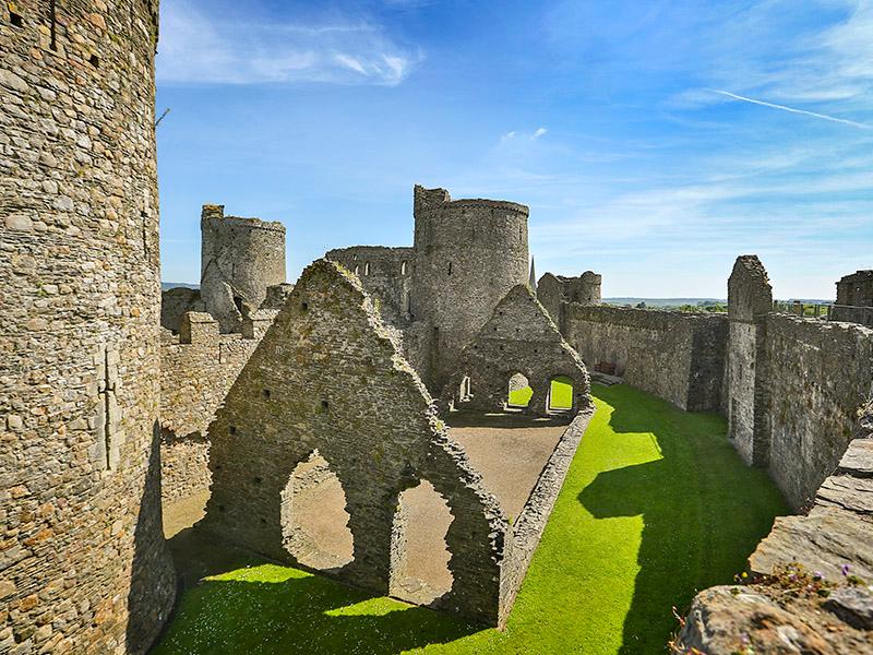 Interior of Kidwelly Castle, draped in shadow on a clear day with bright blue sky in the background