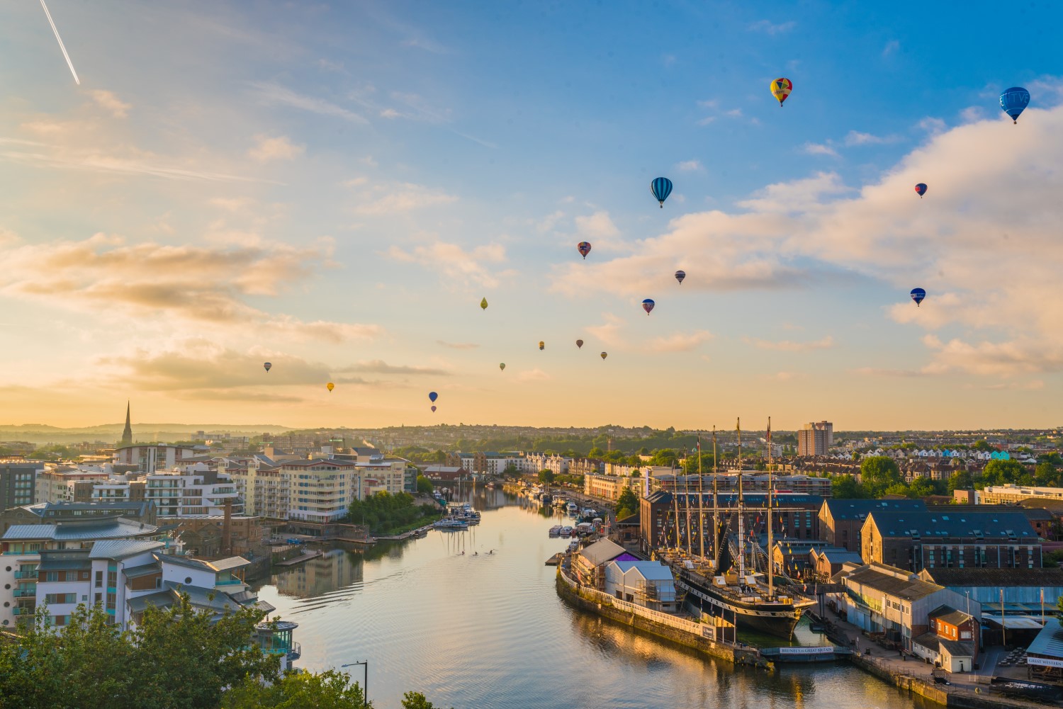 View of Bristol during the International Balloon Fiesta, with hot air balloons rising into the sky on a clear day.