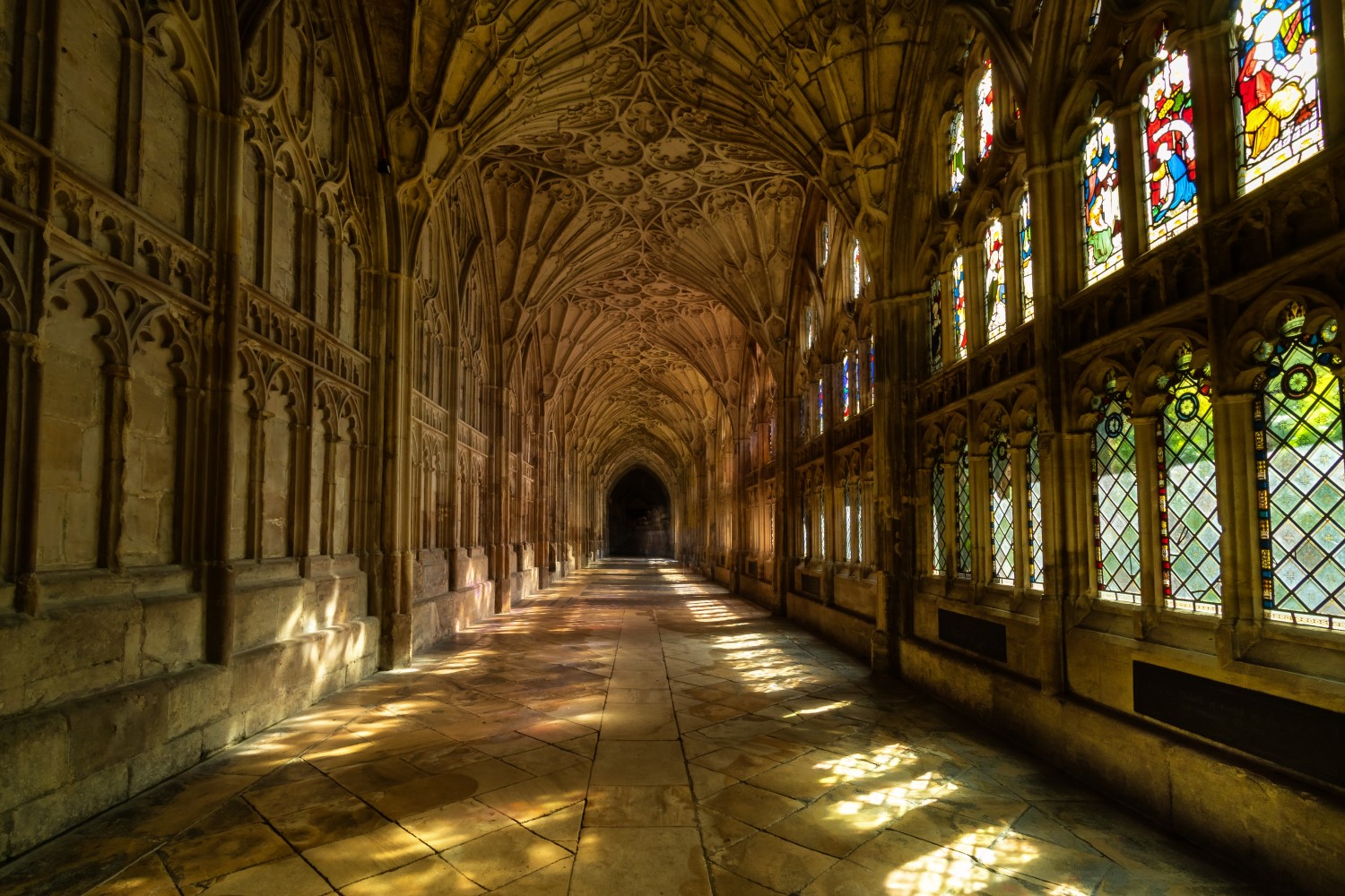 Interior shot from Gloucester Cathedral, with light from stained glass windows illuminating a long hallway