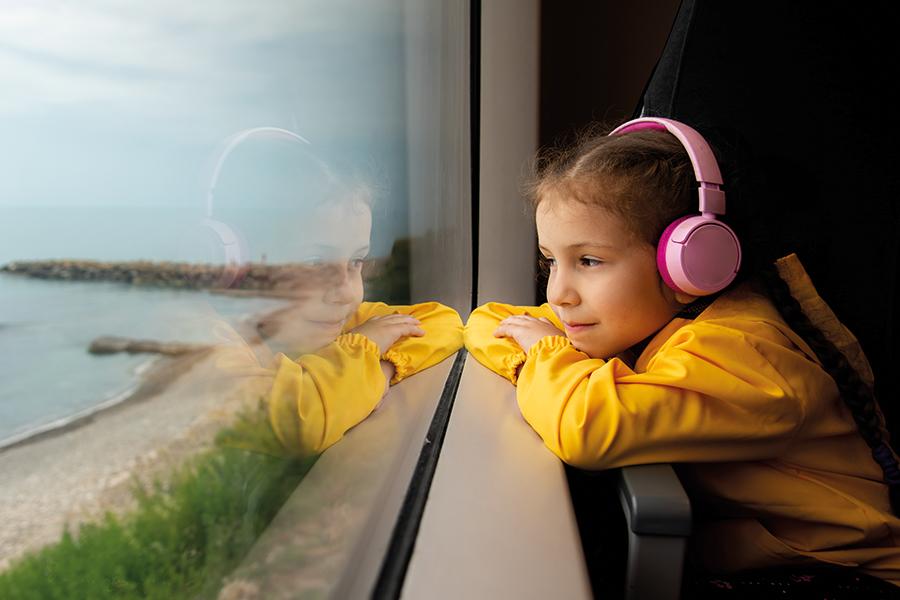 A child with pink headpohones staring out of the window on their train journey.