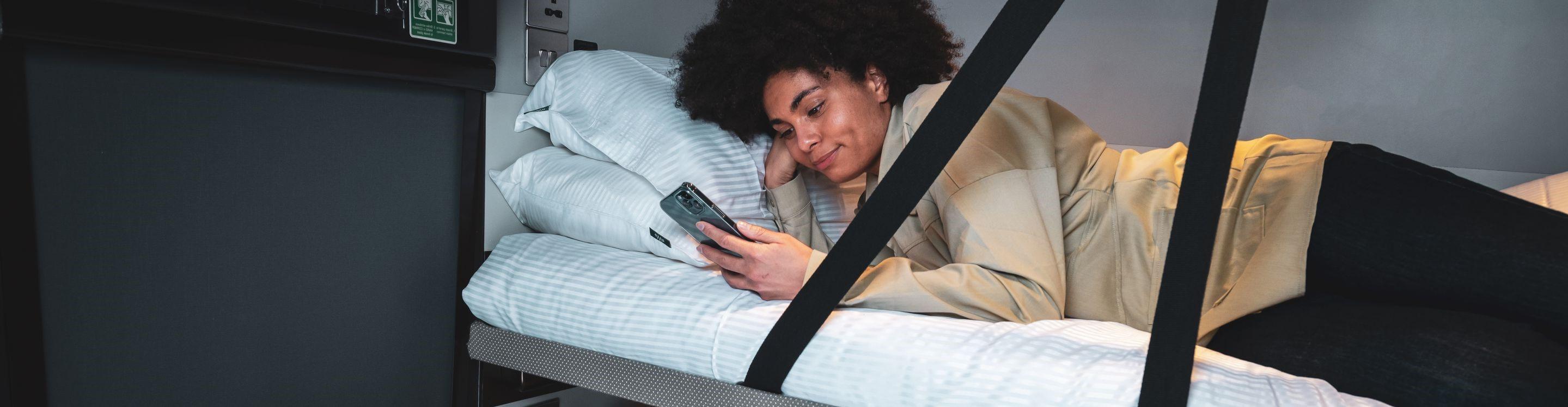 Photograph of a woman on a sleeper service looking at a smart phone 