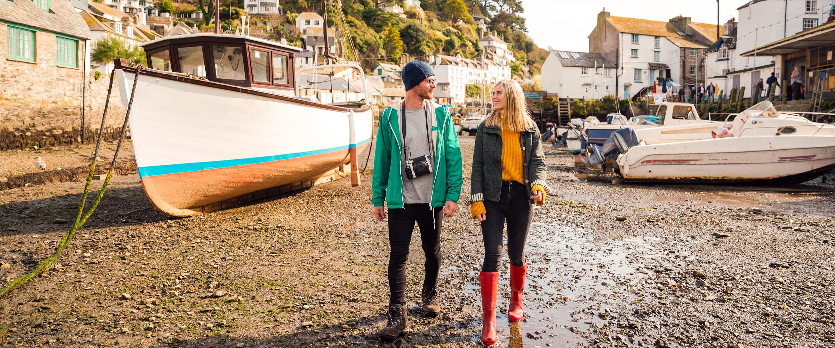 Two people walking through a harbour with the tide out in a small fishing village.