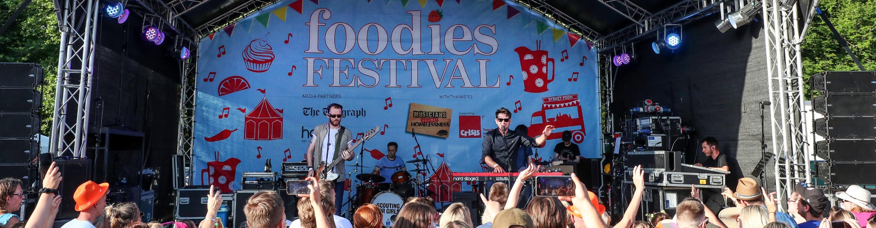Photo of a band playing to audience on stage at Foodies Festival 