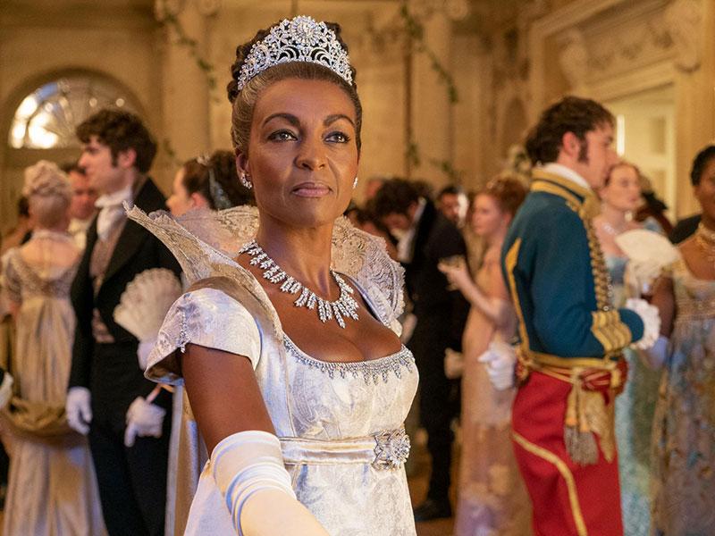 Adjoa Andoh performing as Lady Danbury in the Netflix series Bridgerton, seen here in a white ballgown and tiara, with guests in the background, filmed on location in Bath, Somerset, UK