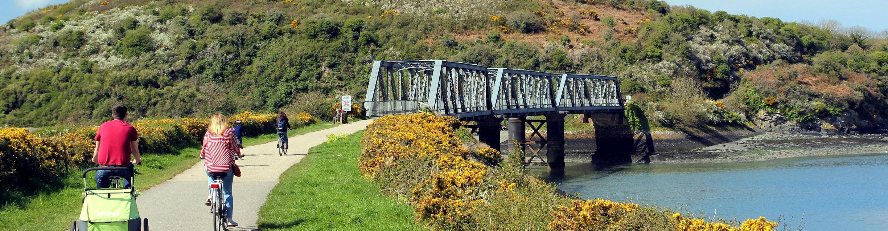 Cyclists approaching a disused iron railway bridge on the Camel Trail, near the Camel Estuary, Cornwall, UK