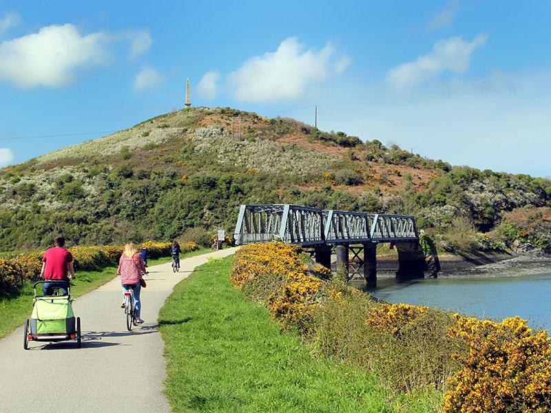 Cyclists approaching a disused iron railway bridge on the Camel Trail, near the Camel Estuary, Cornwall, UK