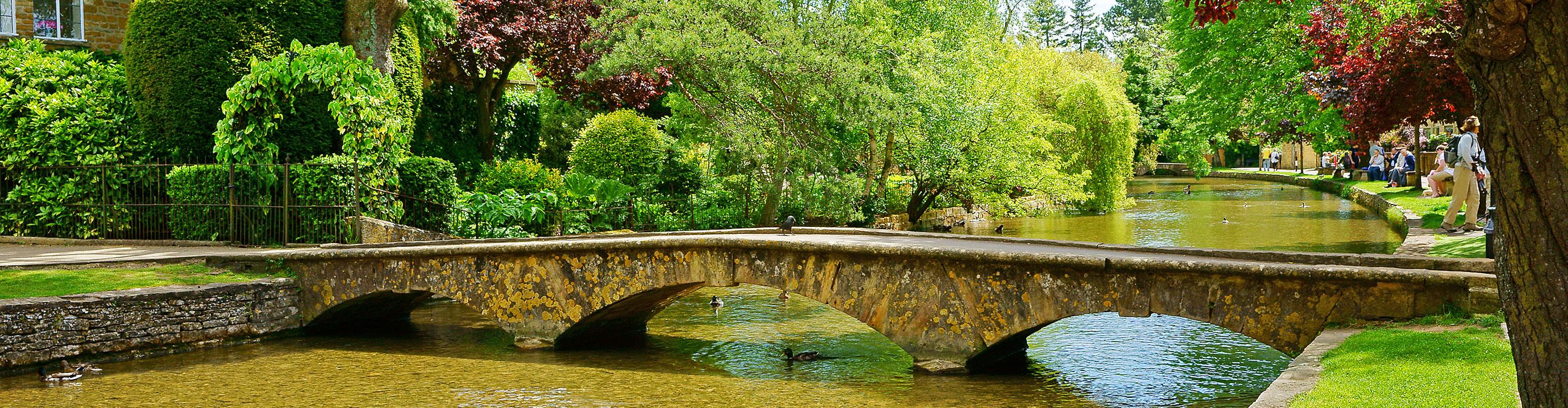 The River Windrush flowing through Bourton-on-the-Water, with a low bridge and trees overhanging the water, UK