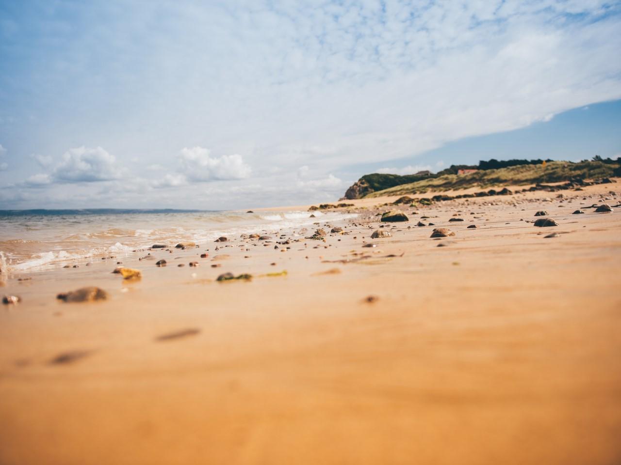 Long landscape shot of a golden beach, showing the shore and sky, with a bank out of focus in the distance.