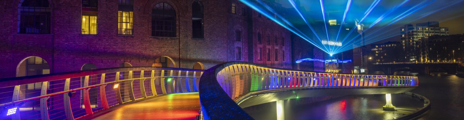 Bridge illuminated in different colours over the water at night, as part of Bristol Light Festival. Image credit: Andre Pattenden.