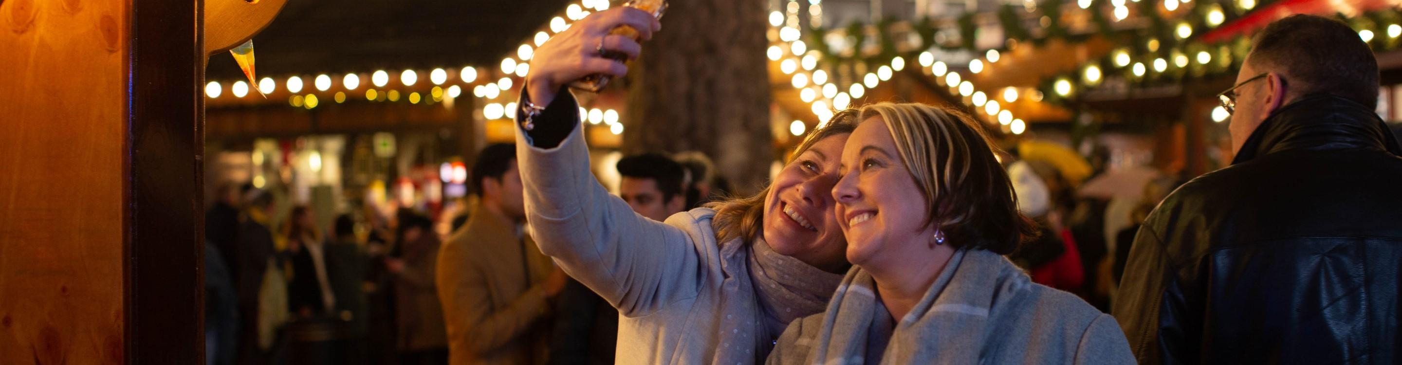 Two people smiling as they take a selfie at a Christmas market