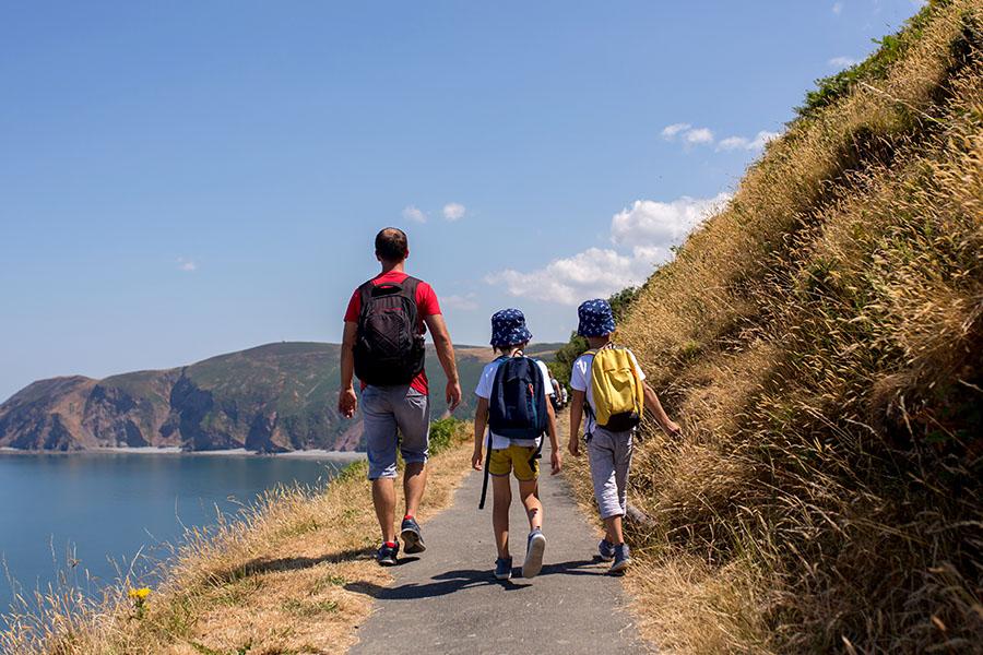 Photo of a family from behind, walking across a coastal path in the summer
