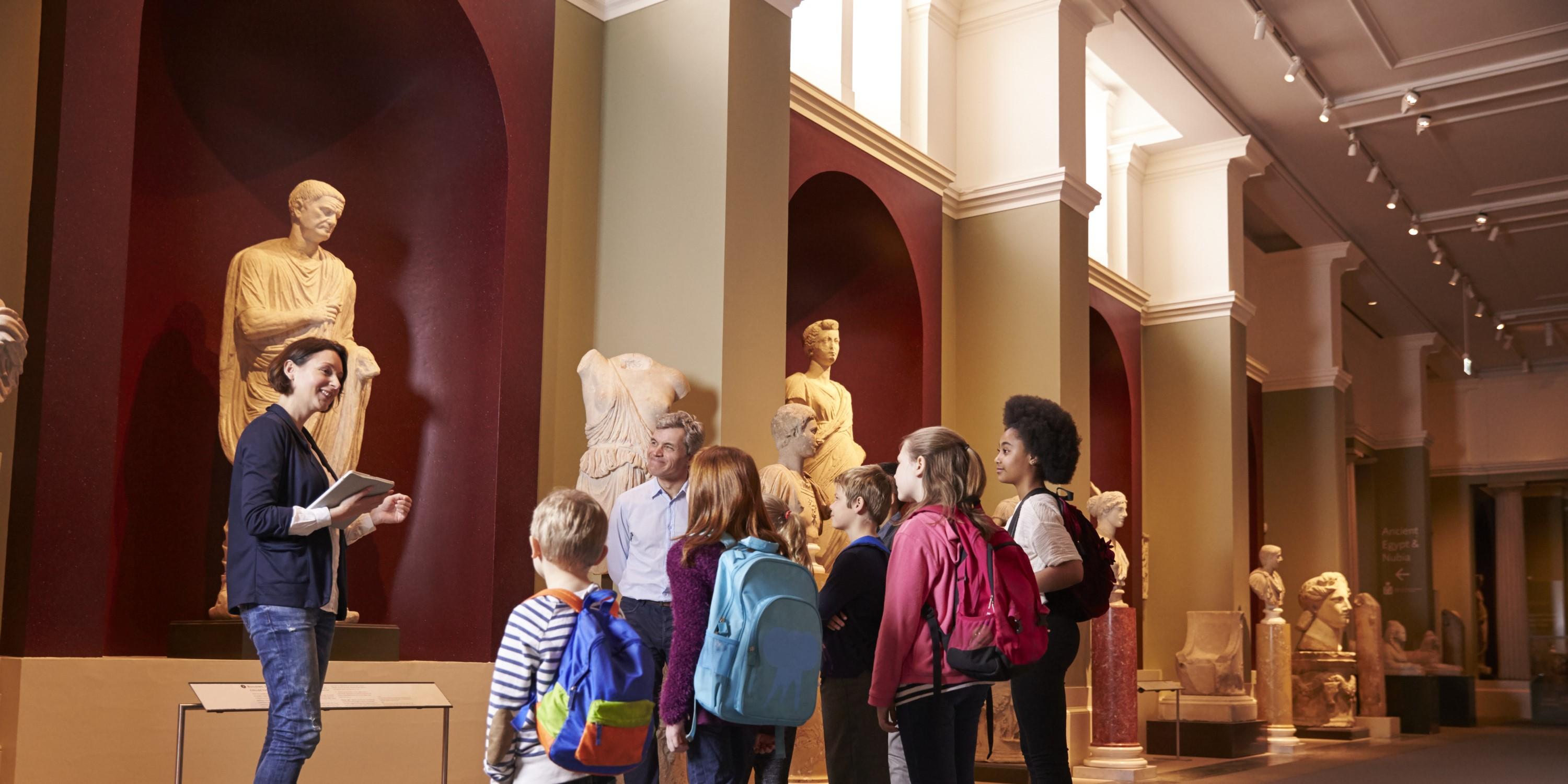 A guide or teacher showing a group of attentive children around a museum.