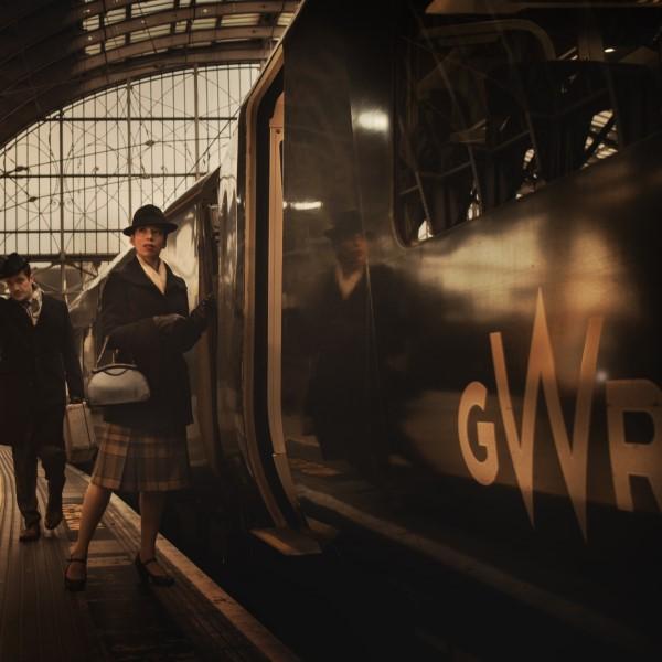 Stylised photo of actors from Agatha Christie's The Mousetrap in full period costume, boarding a GWR train.