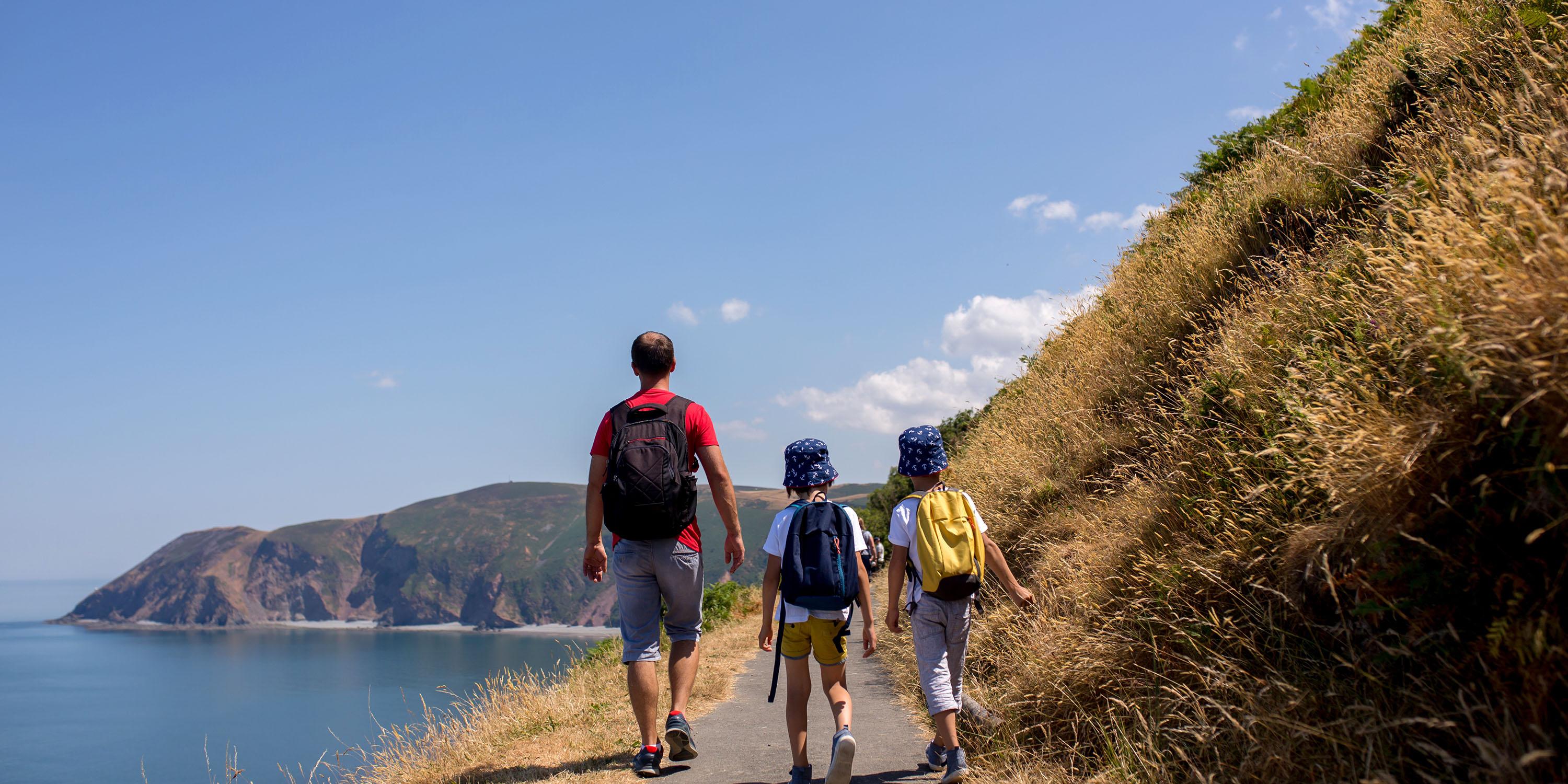 Photo of a family from behind enjoying a hike along a coastal path in summer