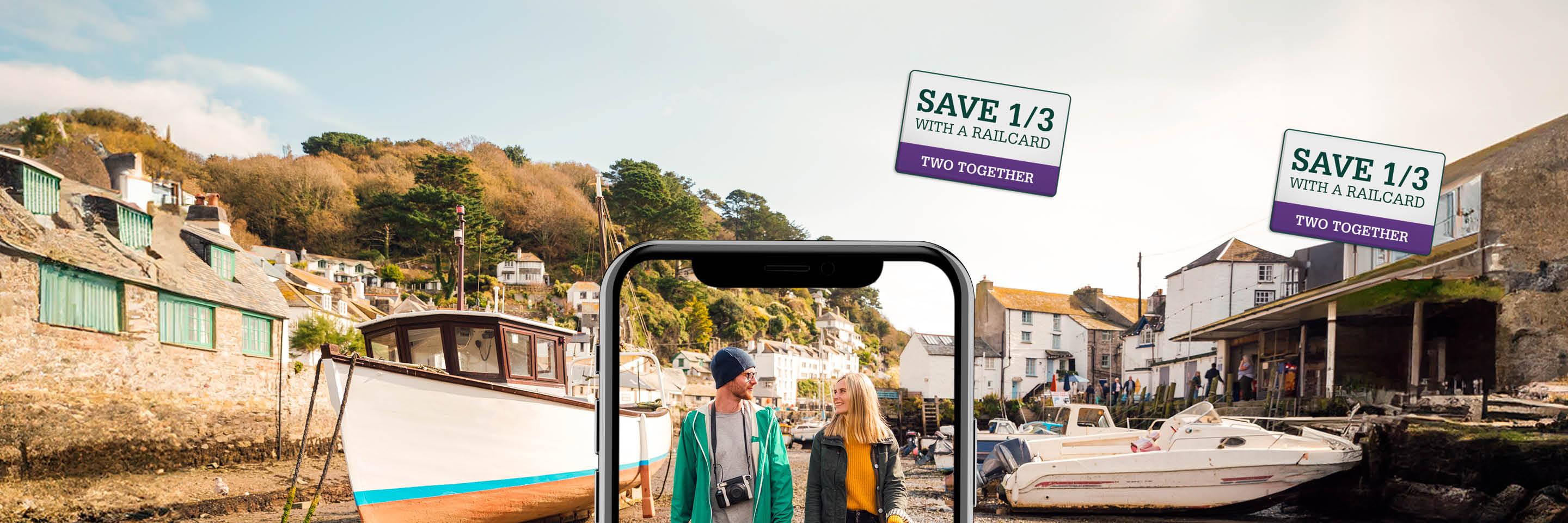 Two people walking through a small seaside village, lined by small boats. The two people are framed in a phone screen, with the caption 'Save one third with a Railcard: Two Together'.