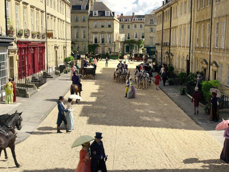 A still from the opening scenes of Netflix's Bridgerton, episode 1, showing Albert Street, Bath, UK. Characters are wearing period dress and riding horses and carts