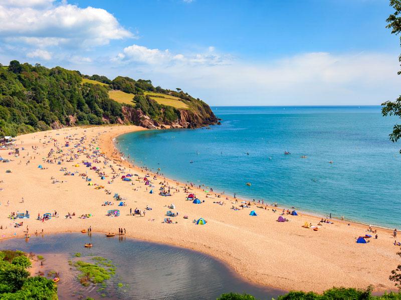 A sunny seascape with people enjoying the beach in Blackpool Sands, Devon, UK