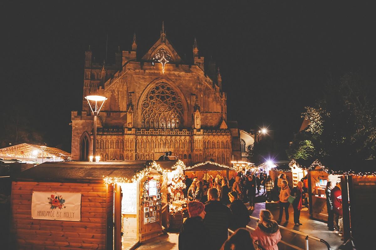 Christmas stalls at the Exeter Christmas Market, framed against Exeter Cathedral at night