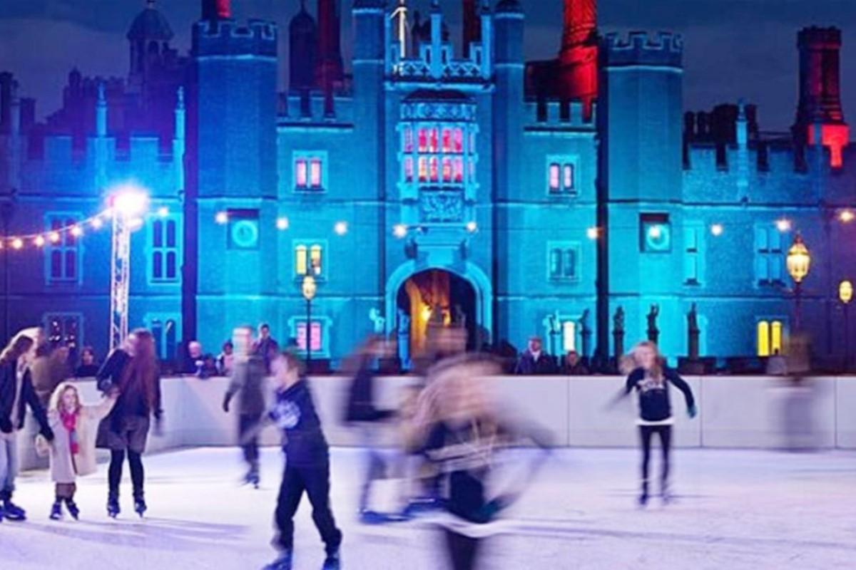 Photo of people ice skating at Hampton Court Palace, with the Palace lit with blue lighting in the background.