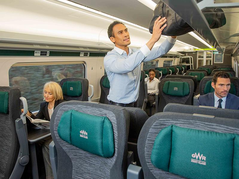 Passenger stowing luggage away in GWR's First Class carriage